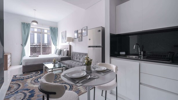 Een moderne hotelkamer met een bed, een bank, een eettafel, stoelen en een kitchenette.