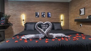 A hotel room with a brick wall, a bed with a black bedspread, and a heart-shaped towel arrangement on the bed. - Aconchego Casa 01 Ofur Lareira e Sala de Cinema (Braganca Paulista)
