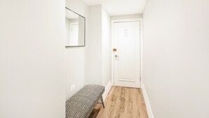 A narrow hallway with a wooden floor, a white door, and a bench with a geometric-patterned cushion. - Upper west side 3 bedroom retreat (New York)