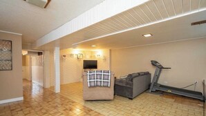 A spacious living area with a wooden floor, a gray sofa, a treadmill, and a brick wall with a flat-screen TV. - Spacious 1 bedroom apartment, excellent location, separate entrance,safe & clean (Toronto)