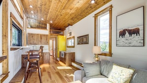 A cozy interior with a wooden ceiling, a dining area with chairs, a sofa with a map cushion, and a kitchen with yellow cabinets. - Tiny in Paradise! Near Chico and SAGE Lodge! (Pray)