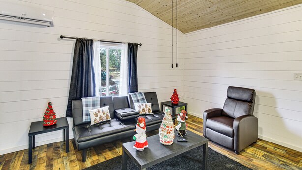 Ein Wohnzimmer mit einem schwarzen Ledersofa, einem braunen Ledersessel, einem Couchtisch mit Weihnachtsdekoration und einem Fenster mit Vorhängen.