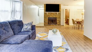 Ein Wohnzimmer mit einer Couch, einem Couchtisch, einem Kamin und einem an der Wand befestigten Fernseher.