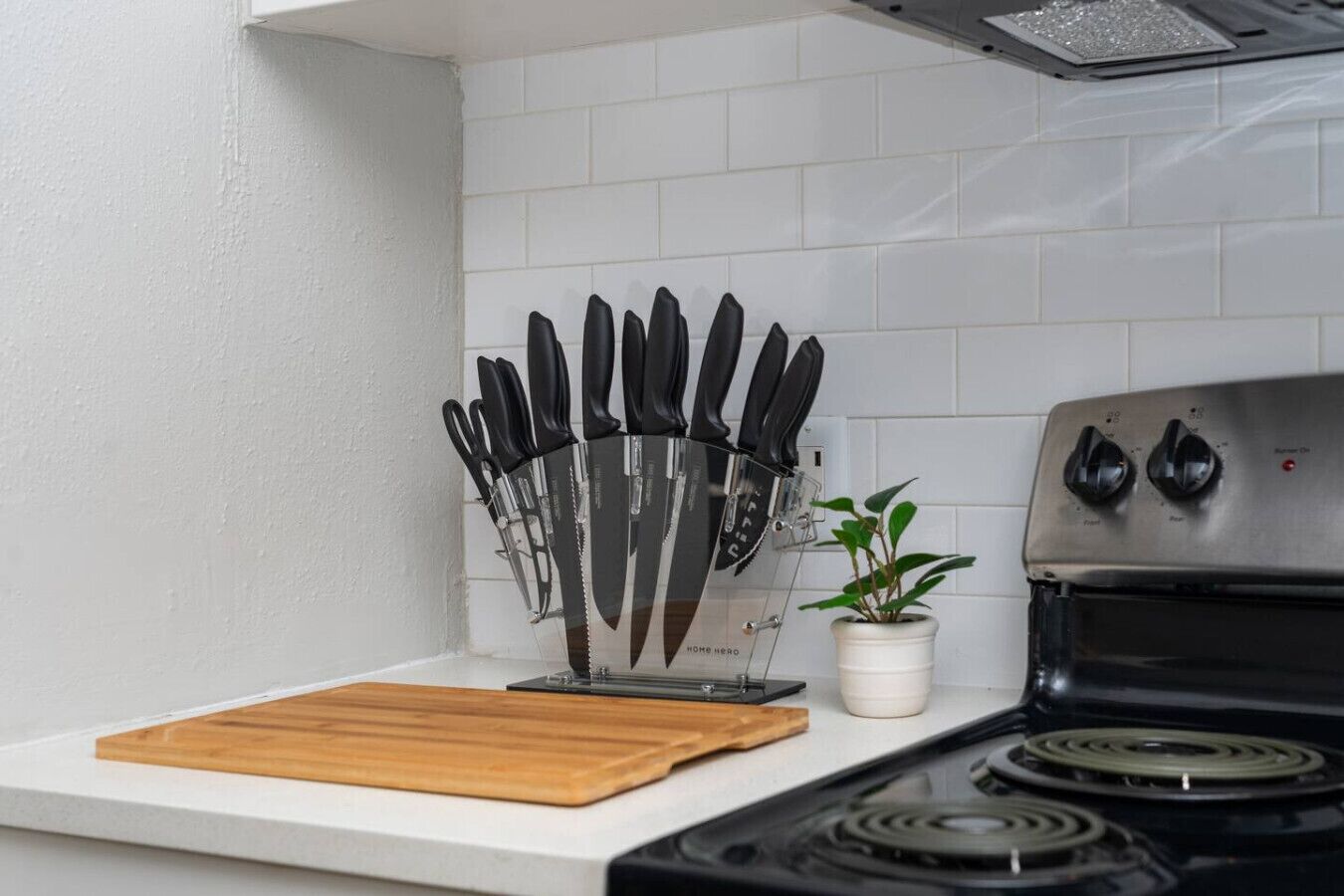 A kitchen with a knife block, a wooden cutting board, a stove, and a potted plant.