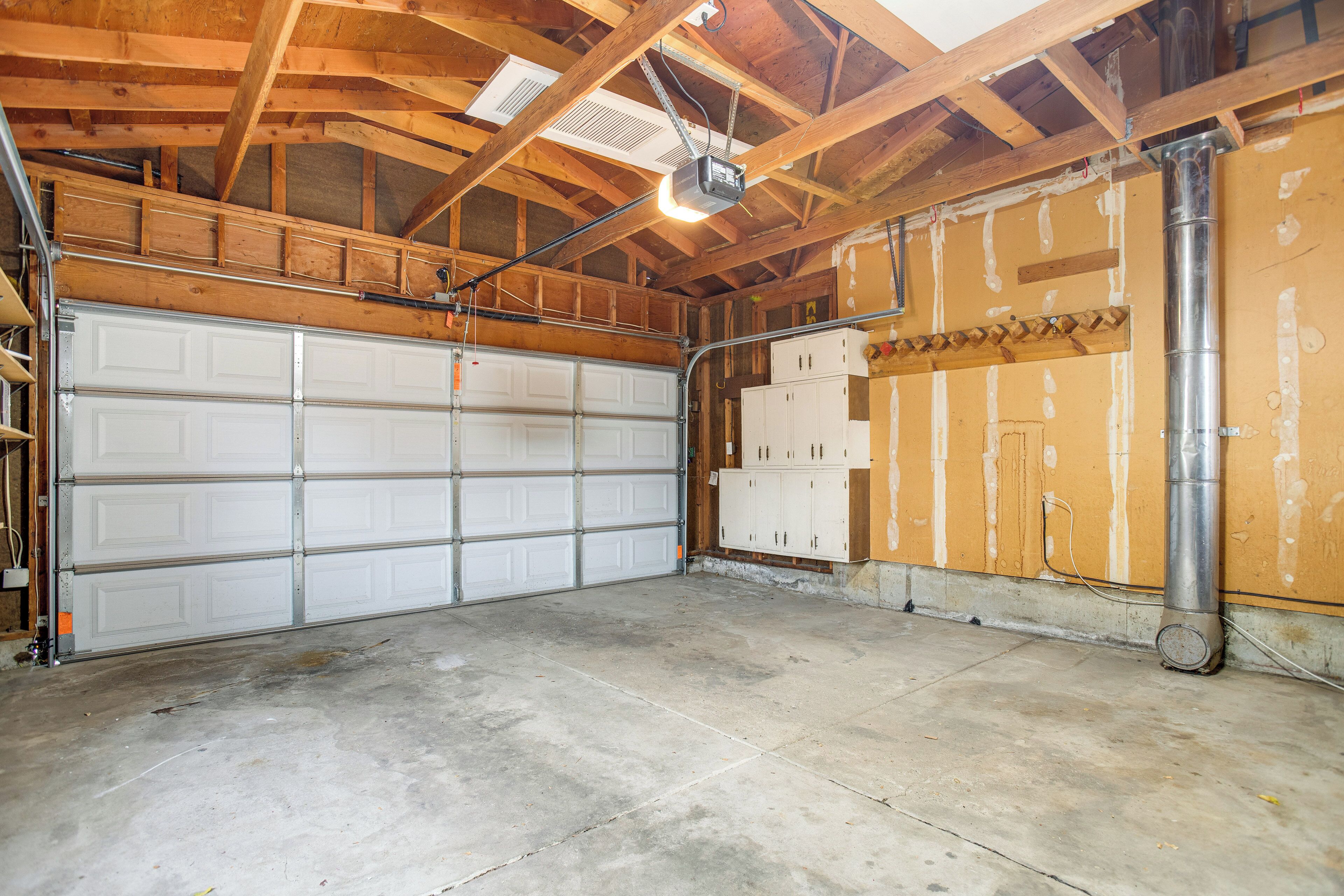 A garage with a white garage door, wooden beams, and a ceiling vent.