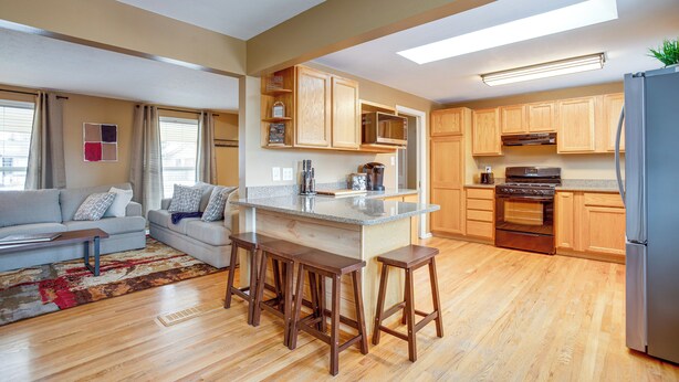 A modern kitchen with wooden cabinets, a central island with stools, and a built-in oven. - Gather Family! Home w/ Fenced Yard in Wheat Ridge (Wheat Ridge)