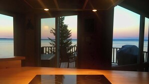 A kitchen with a view of the ocean, a wooden table, and a grill outside. - Le P'tit Bijou au Bord du Fleuve (Saint-Siméon)