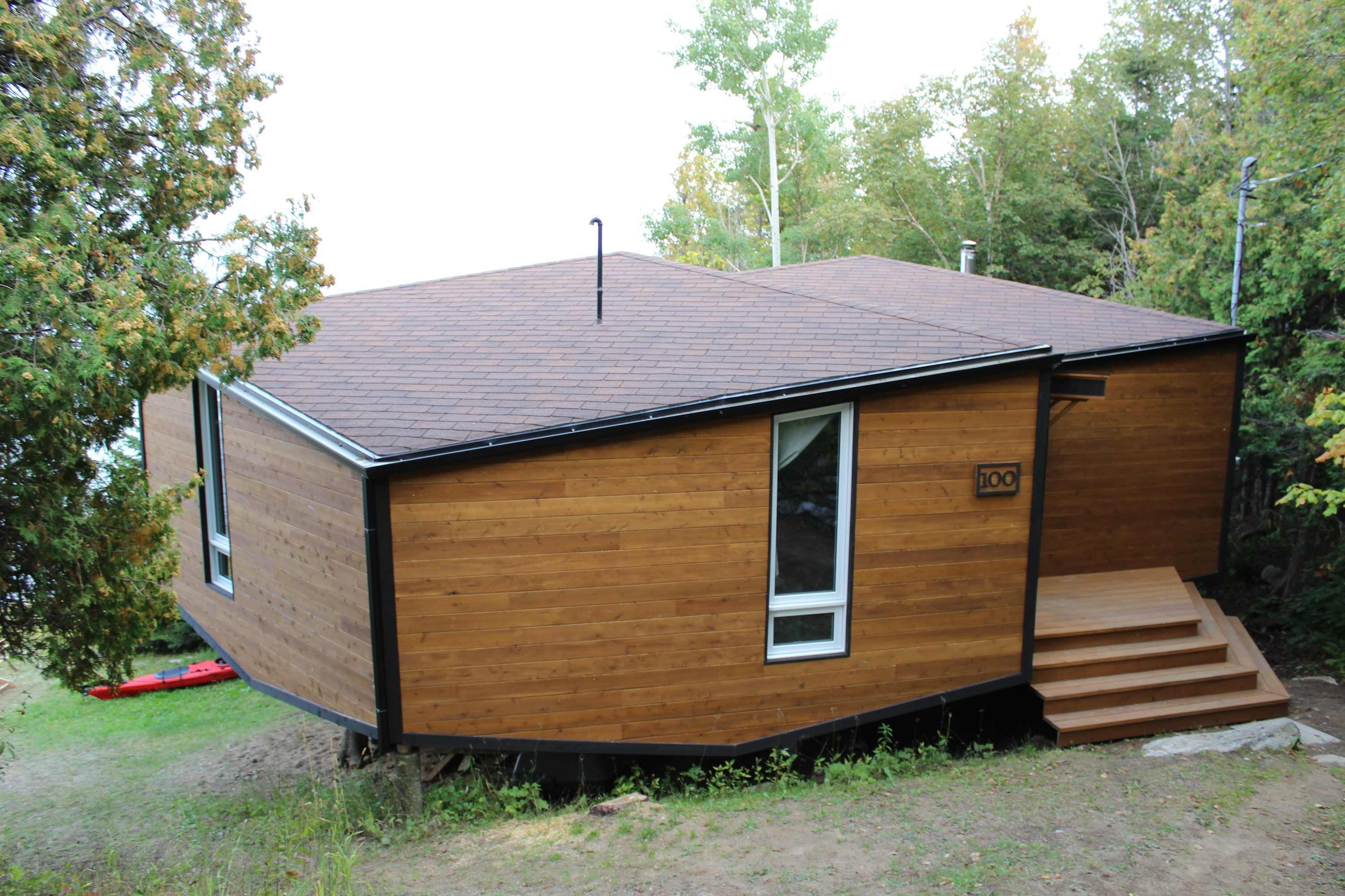 A small, wooden cabin with a sloped roof, a single visible window, and a door with a number plate.
