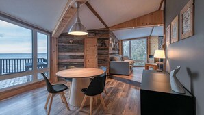 A modern interior with a wooden dining area, a sofa, and a view of the ocean. - Le P'tit Bijou au Bord du Fleuve (Saint-Siméon)