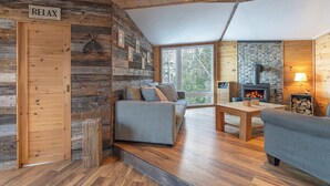 A cozy cabin interior with a wooden wall, a sofa, a table, and a fireplace. - Le P'tit Bijou au Bord du Fleuve (Saint-Siméon)