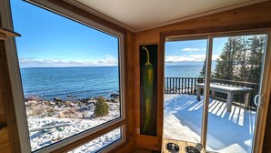 A wooden cabin with large windows overlooking a snowy landscape and a body of water. - Le P'tit Bijou au Bord du Fleuve (Saint-Siméon)
