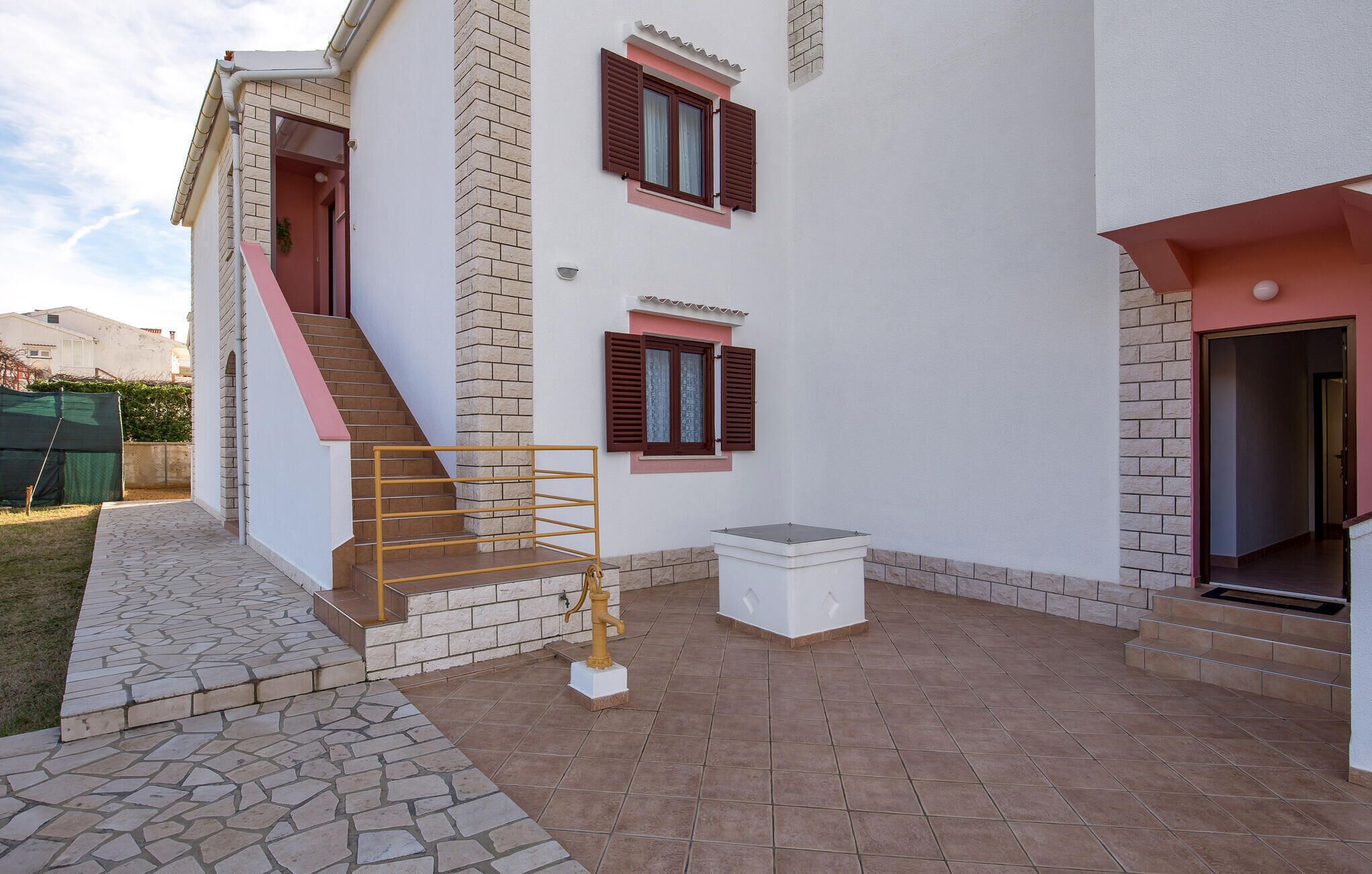 Ein zweistöckiges Haus mit Treppe, einer kleinen Außen-Sitzgelegenheit und einer Springbrunnen.