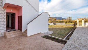 Ett modernt hus med en trappa som leder till en dörr, en liten trädgård och utsikt över berg i bakgrunden.