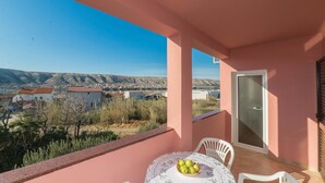 Ein Balkon mit Tisch, Stühlen und einer Obstschale. Durch den Balkon ist eine Aussicht auf eine Stadt und Berge sichtbar.