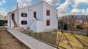 Ein weißes, zweistöckiges Haus mit kleinem Vorgarten, einer Treppe und Blick auf die Berge.
