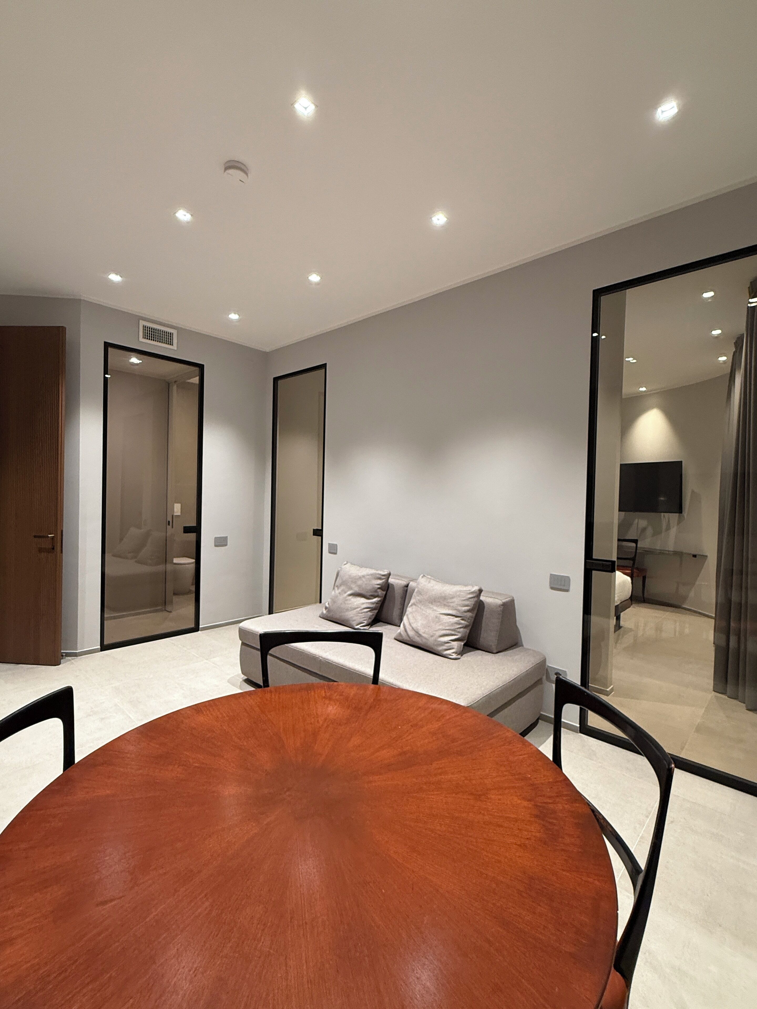 A modern room with a round wooden table, a sofa with cushions, and a glass partition.