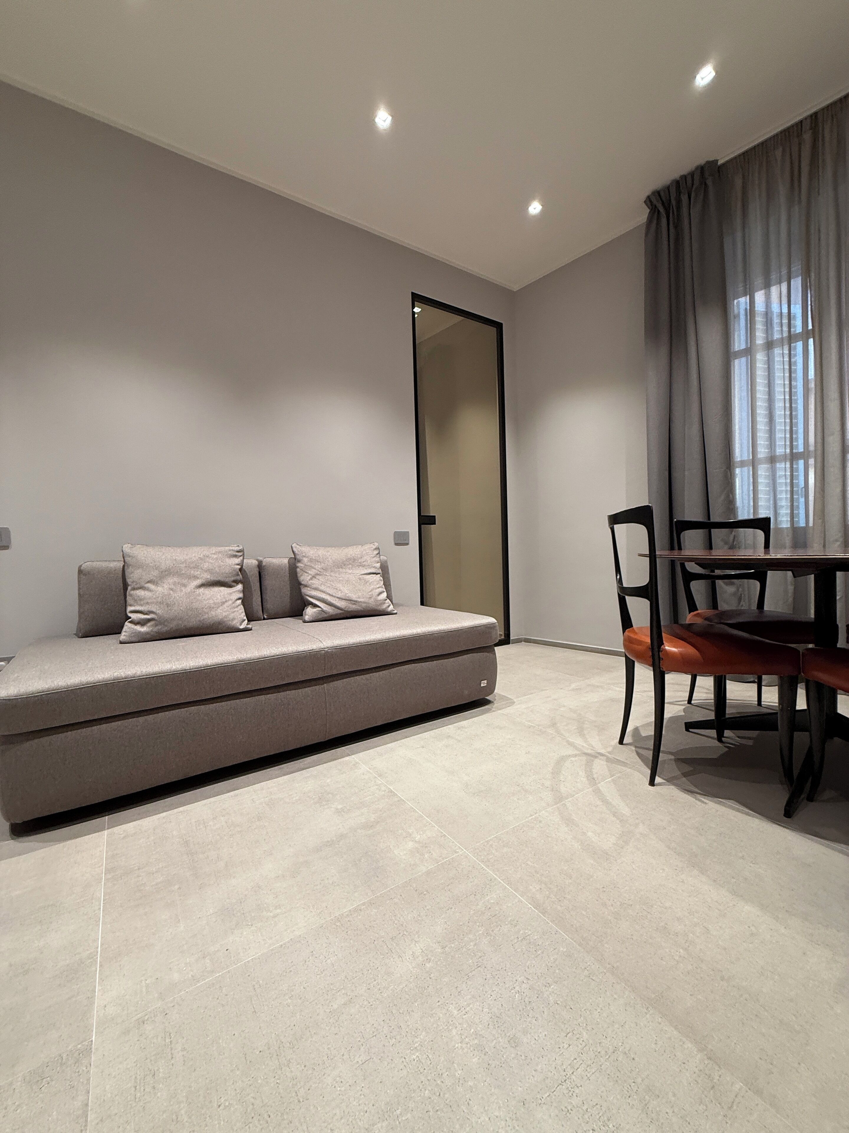 Una sala de estar moderna con un sofá, una mesa de comedor con sillas y un ventanal con cortinas.