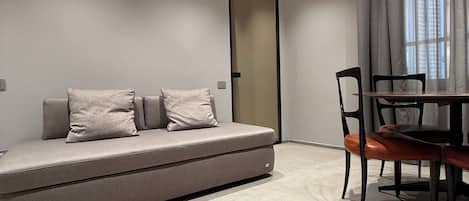 Una sala de estar moderna con un sofá, una mesa de comedor con sillas y un ventanal con cortinas.