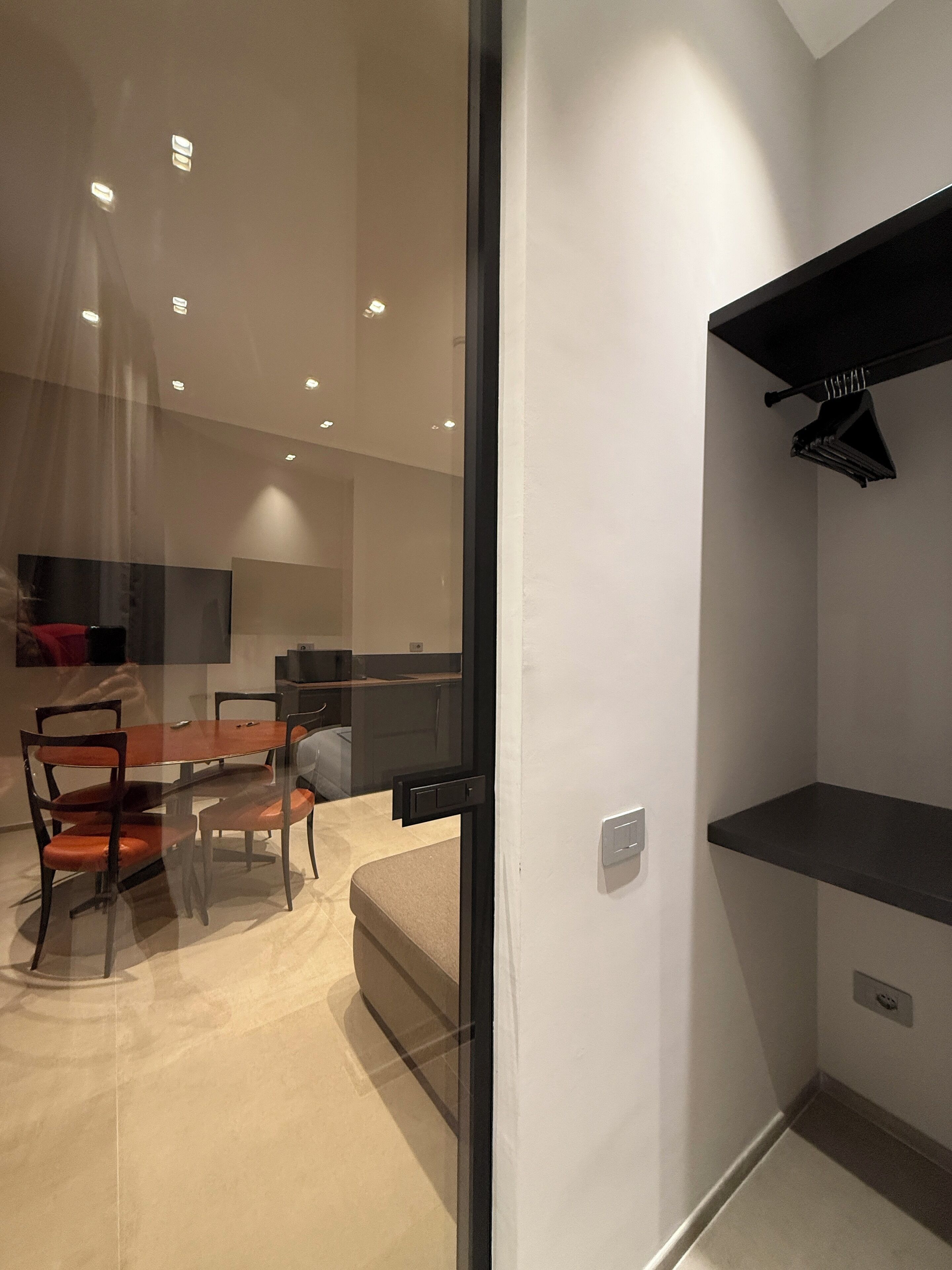 A modern kitchen with a dining area, featuring a glass partition, a built-in oven, and a black countertop.