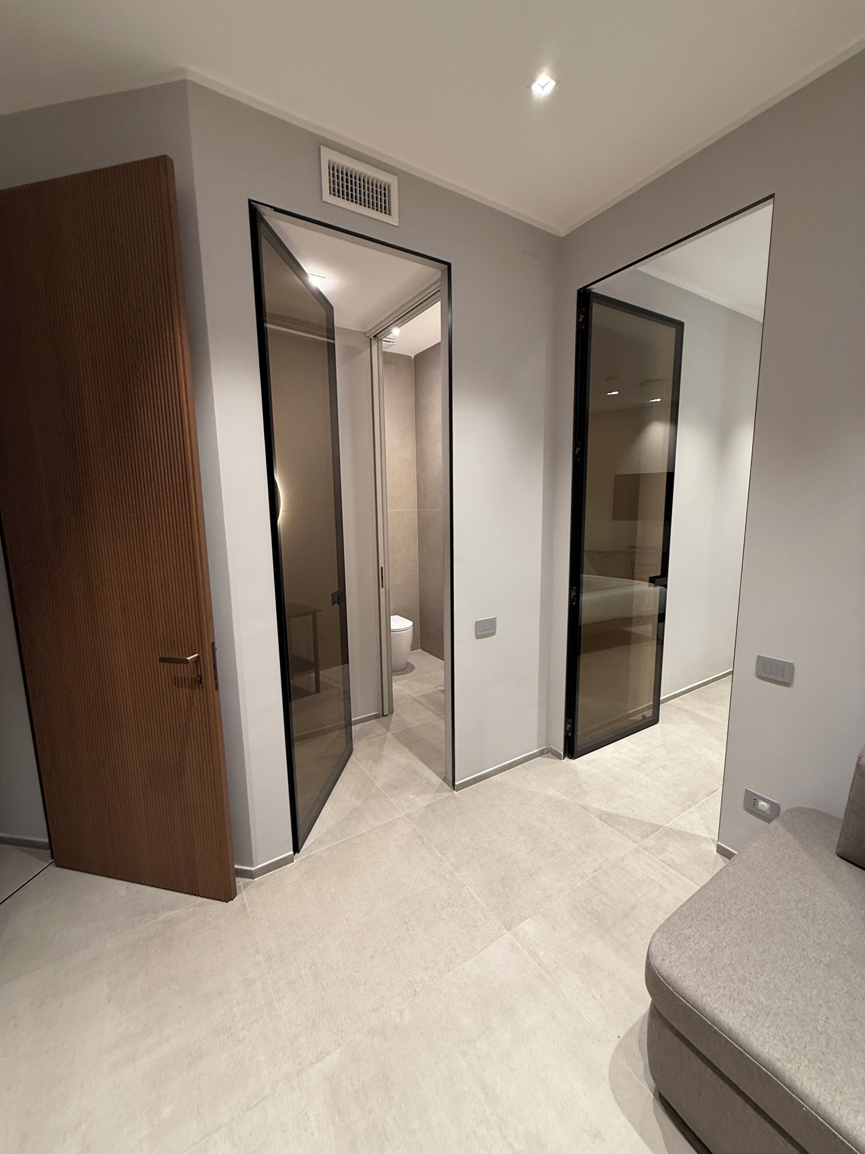 A modern hotel room with a large mirror, a wooden door, and a beige carpet.