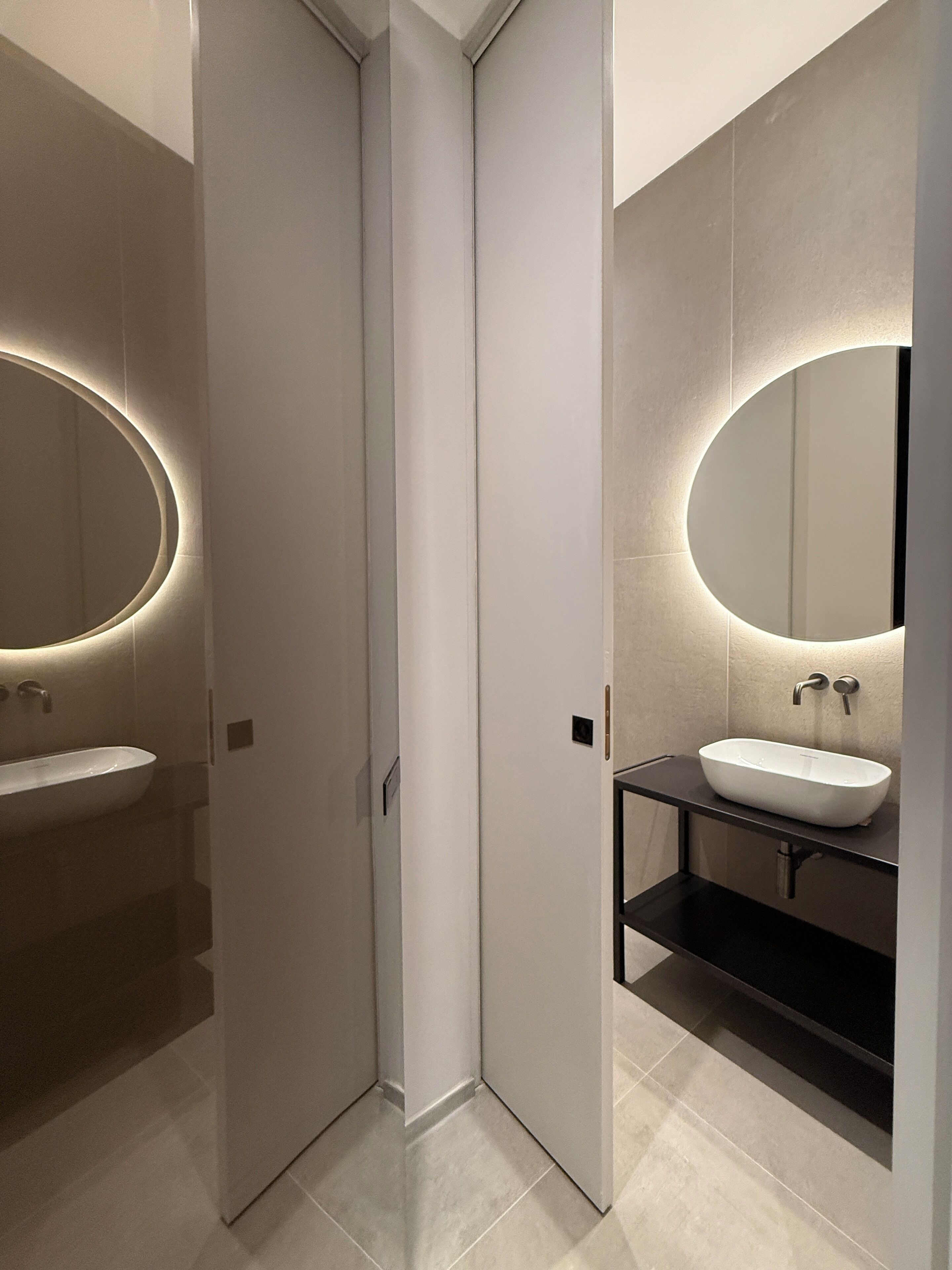 A modern bathroom with a white sink, a round mirror, and a black countertop.