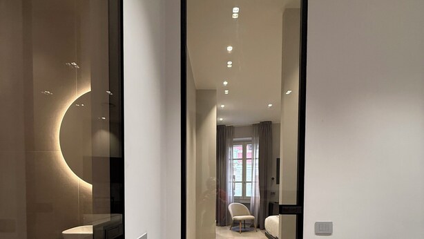 A modern hotel room with a glass partition, a round light fixture, a sofa, and a bed. - LEOPOLDO SUITES (Cagliari)