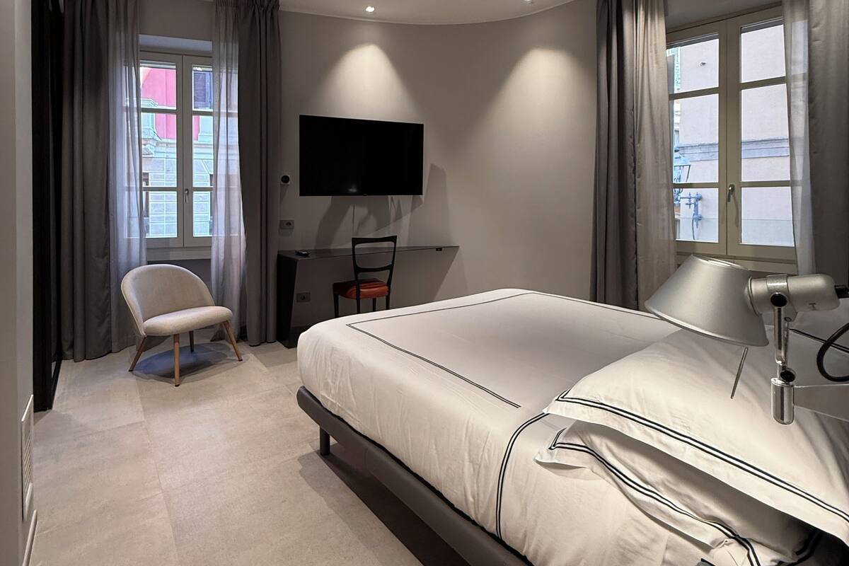 A modern bedroom with a large bed, a desk with a chair, a TV, and a window with curtains.