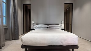A modern bedroom with a large bed, two bedside lamps, and a view of a hallway. - LEOPOLDO SUITES (Cagliari)