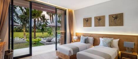 A hotel room with two beds, a large sliding glass door leading to a garden, and artwork on the wall.
