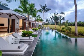 A poolside area with lounge chairs, umbrellas, and a view of a lush landscape. - Villa Florentine by BaliSuperHost (Bali)