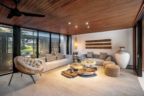 Un salon moderne avec un plafond en bois, une grande fenêtre, un canapé, une table basse ronde et un vase décoratif.