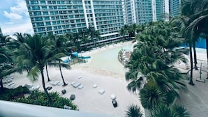 A high-rise hotel with a pool area, palm trees, and beach chairs. - Relaxing 1BR Retreat with Balcony (Paranque)