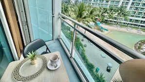 A balcony with a table, chairs, and a potted plant. A view of a high-rise building and a beach with palm trees is visible through the glass. - Relaxing 1BR Retreat with Balcony (Paranque)
