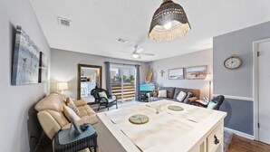 Ein modernes Wohnzimmer mit einer großen Kücheninsel, Ledersesseln, einem Deckenventilator und Blick durch die Glastür.
