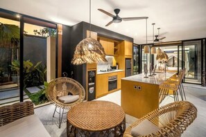 Une cuisine moderne avec des meubles en bois, un îlot central et un coin repas doté de meubles en osier.