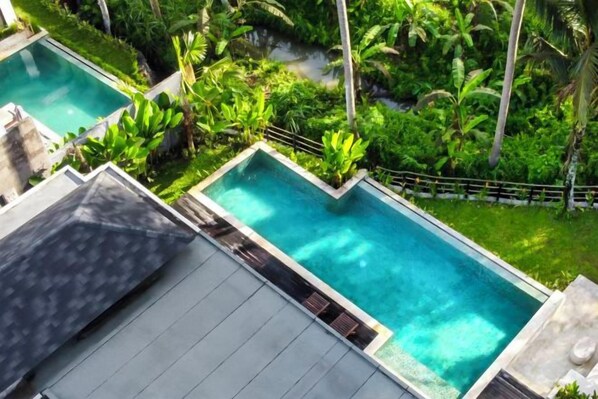 A rectangular pool with a surrounding lush green landscape, including palm trees and other vegetation. - Villa Alba by BaliSuperHost (Bali)