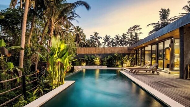 A modern pool area with a wooden deck, lounge chairs, and tropical vegetation. - Villa Alba by BaliSuperHost (Bali)