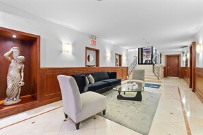 A hotel lobby with a reception desk, a statue, a sofa, and a staircase.