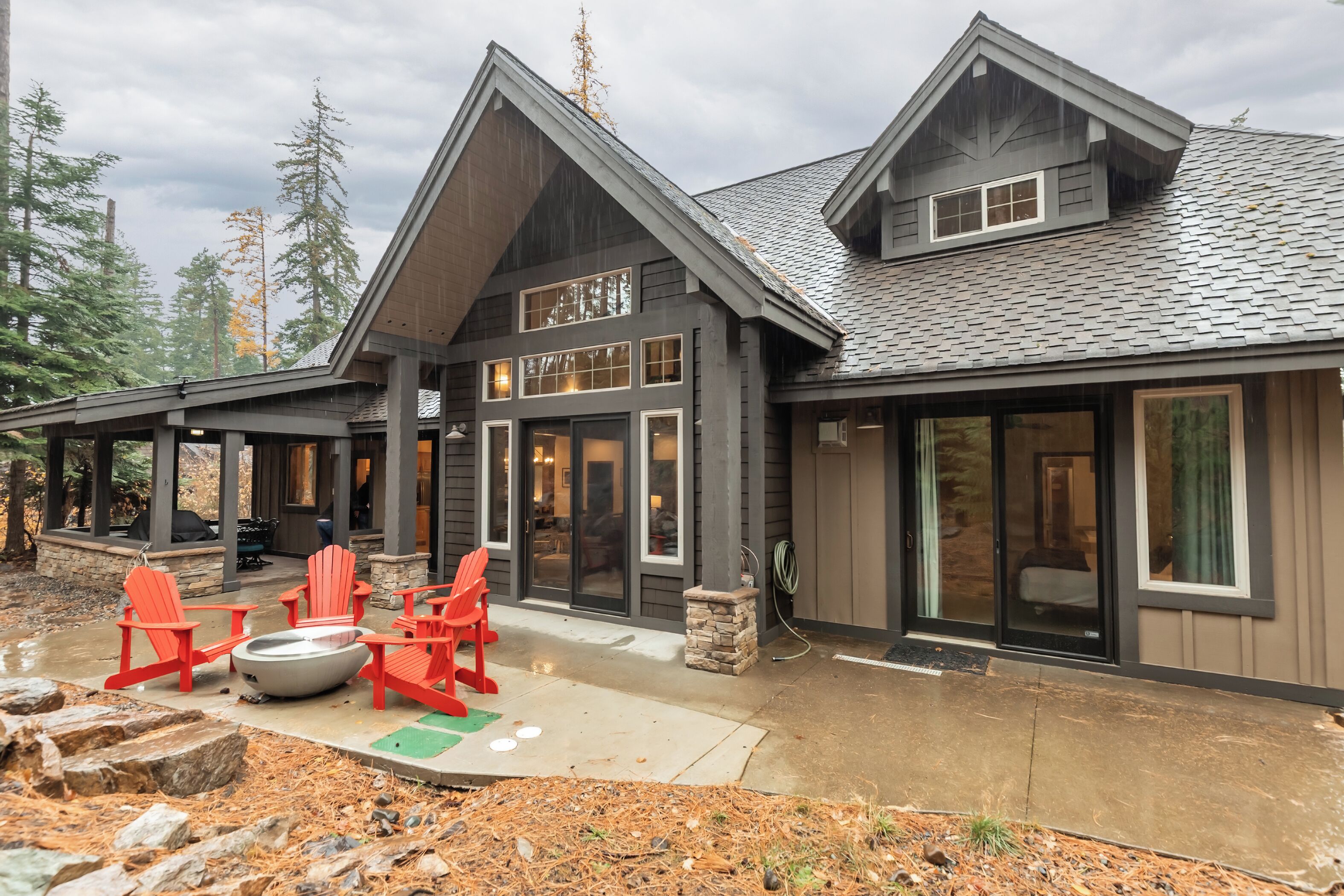 A modern lodge with a large deck, red Adirondack chairs, and a stone fire pit.