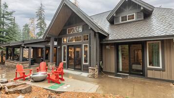 A modern lodge with a large deck, red Adirondack chairs, and a stone fire pit.