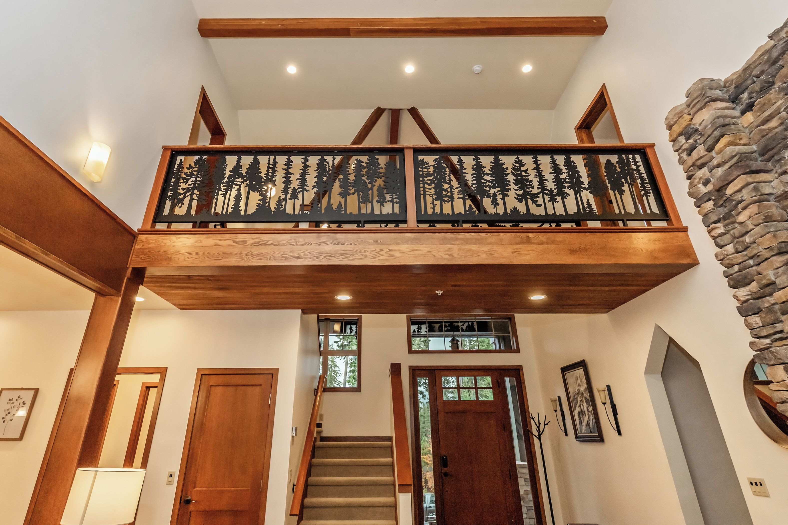Un escalier en bois doté d’un balcon orné d’un motif représentant la silhouette d’une forêt.