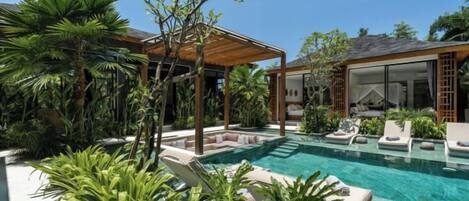 A pool area with lounge chairs, a pergola, and lush greenery.