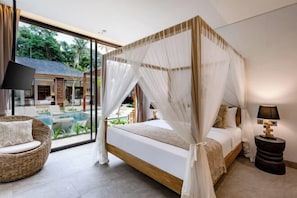 A bedroom with a four-poster bed, a wicker chair, a bedside table, and a view of a pool and outdoor area. - Villa Teva by BaliSuperHost (Bali)