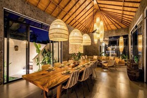 Un comedor con una larga mesa de madera, lámparas colgantes de mimbre y un diseño moderno de techo.