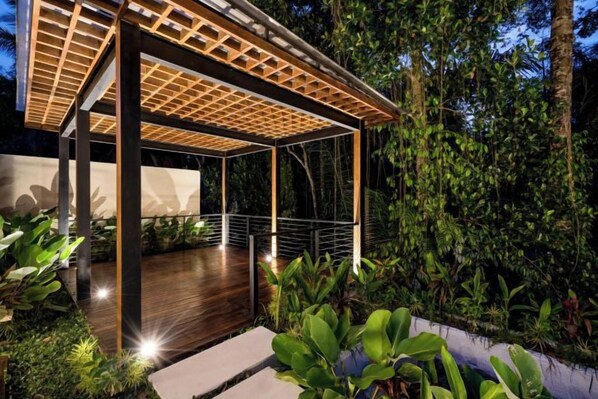 Una estructura moderna al aire libre con terraza de madera, rodeada de abundante vegetación.