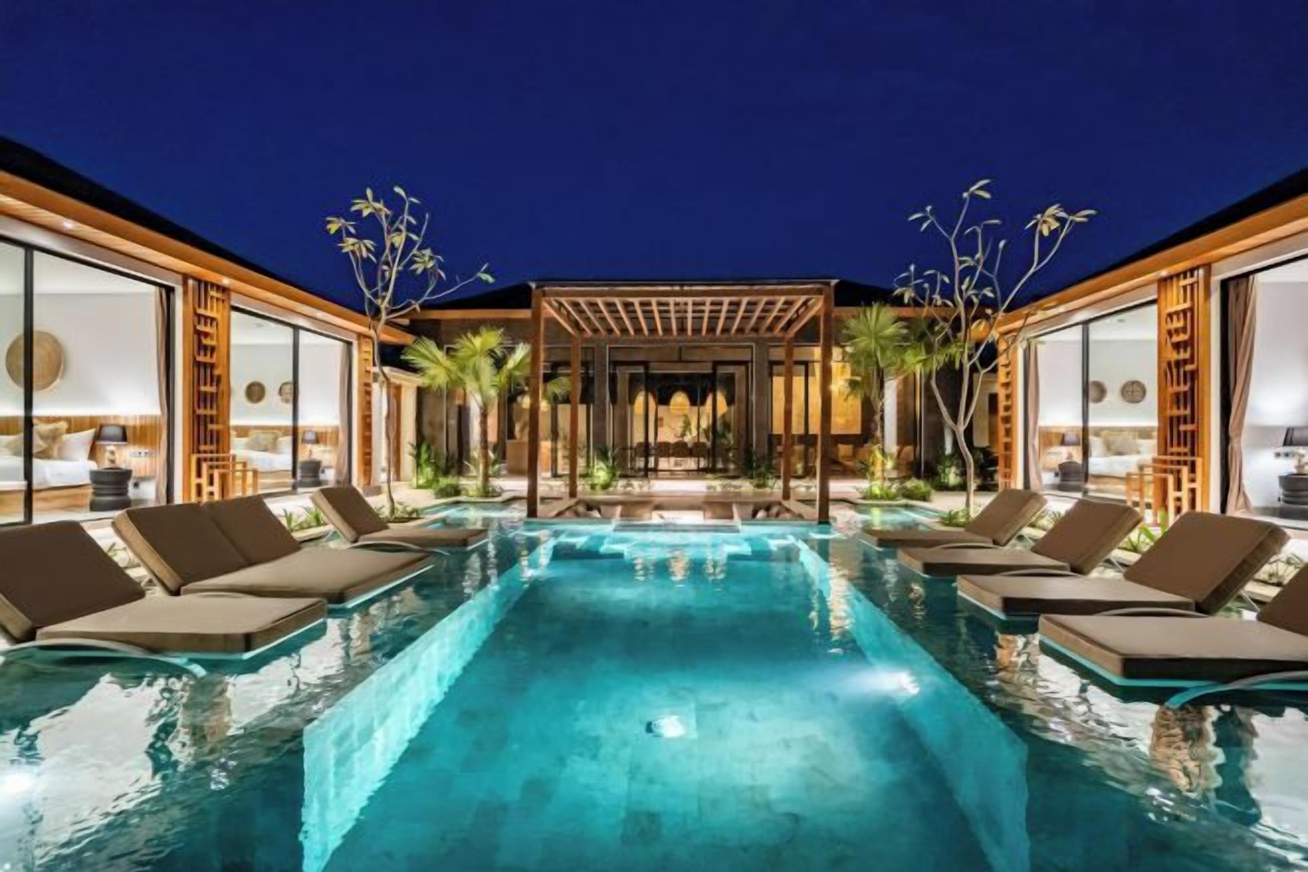 A swimming pool with lounge chairs, a pergola, and a view of a building with large windows.