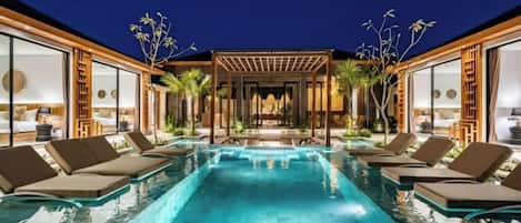 A swimming pool with lounge chairs, a pergola, and a view of a building with large windows.