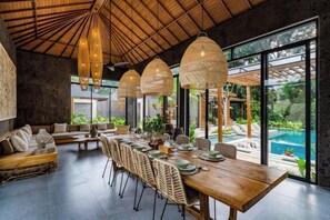 A dining area with a long wooden table, wicker chairs, and hanging light fixtures. - Villa Teva by BaliSuperHost (Bali)
