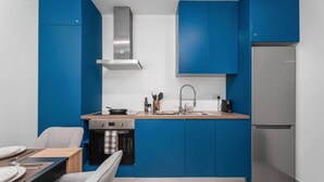 Una cocina compacta con armarios azules, una campana extractora de acero inoxidable, un horno integrado, un lavamanos con un grifo moderno y un refrigerador.