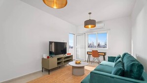 Una sala de estar moderna con un televisor de pantalla plana, un sofá, una mesa de centro y vistas a la ciudad a través de amplios ventanales.